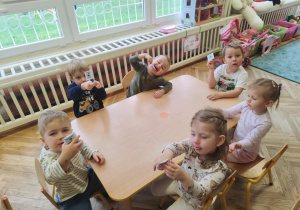 Dzieci siedzą przy stoliku i pokazują lizaki.