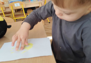 Chłopiec odbija dłoń pomalowaną farbą na papierze.