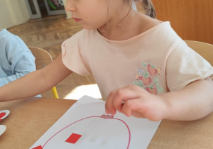 Dziewczynka nakleja kawałki bibuły w kontury jabłka.