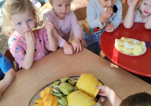 Dzieci jedzą melona, kiwi i kaki.