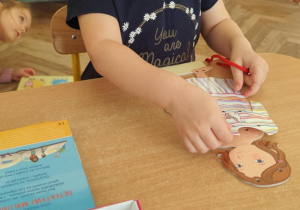 Dziewczynka przewleka sznurek przez otwory.