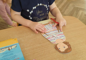 Dziewczynka przewleka sznurek przez otwory.