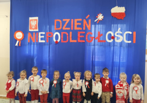 Dzieci pozują na granatowym tle z napisem Dzień Niepodległości.
