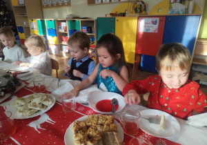 Dzieci próbują ryby, pierogów i kapusty z grochem.