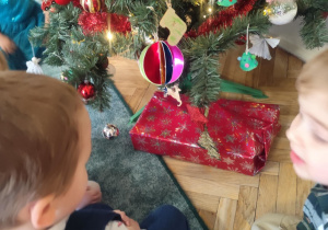 Dzieci odkrywają prezent ukryty pod choinką.