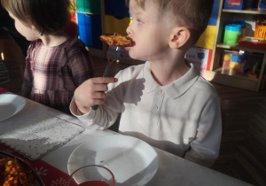 Dzieci próbują ryby, pierogów i kapusty z grochem.