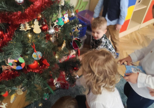 Dzieci odkrywają prezent ukryty pod choinką.