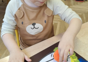 Chłopiec odbija gąbeczkę z farbą na kolorowym kartonie.