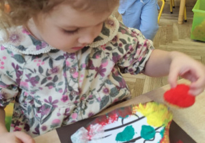 Dziewczynka odbija gąbeczkę z farbą na kolorowym kartonie.