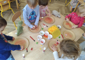 Dzieci naklejają składniki pizzy na papierowy talerzyk.