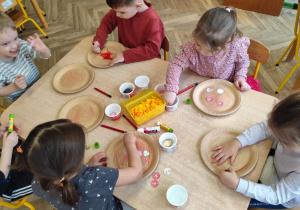 Dzieci naklejają składniki pizzy na papierowy talerzyk.
