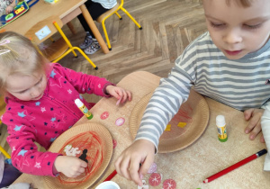 Dzieci naklejają składniki pizzy na papierowy talerzyk.