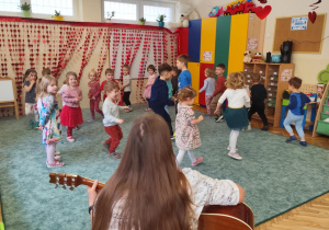 Dzieci bawią się do piosenki granej na gitarze.