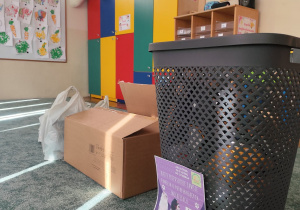 Na zdjęciu widać kosz na dary od chętnych rodziców, plakat tematyczny oraz pudełko na karmę.