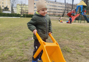 Chłopiec jedzie taczką po ogrodzie.