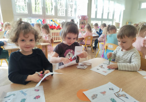 Dzieci wycinają ilustracje owadów.