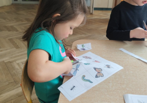 Dzieci wycinają ilustracje owadów.