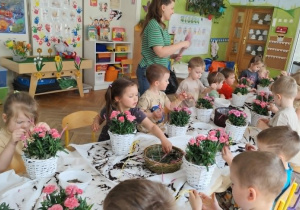 Dzieci wsadzają goździki do wiklinowych koszyczków.