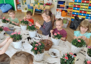 Dzieci wsadzają goździki do wiklinowych koszyczków.